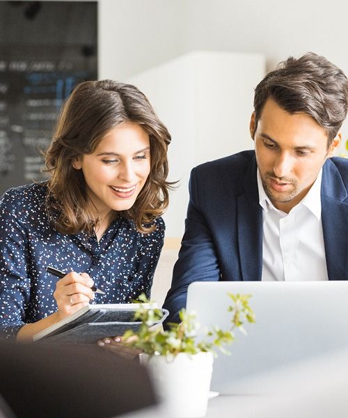 Job bei K-Plus: Personalkauffrau mit Notizbuch und Personalkaufmann sitzen gemeinsam vor Laptop